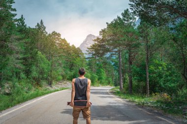 Genç hippi elinde havalı bir uzun tahta tutuyor. Güzel bir seyahat konsepti. Milenyum macera yolculuğu. Kaykay kaykay gezisi. Vahşi doğada spor.