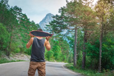 Genç hippi elinde havalı bir uzun tahta tutuyor. Güzel bir seyahat konsepti. Milenyum macera yolculuğu. Kaykay kaykay gezisi. Vahşi doğada spor.