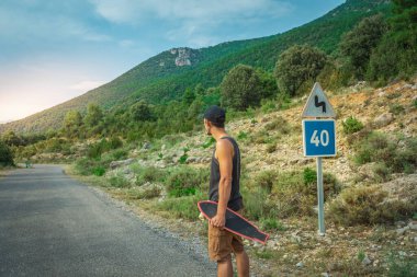 Genç hippi elinde havalı bir uzun tahta tutuyor. Güzel bir seyahat konsepti. Milenyum macera yolculuğu. Kaykay kaykay gezisi. Vahşi doğada spor.