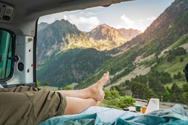 Gün batımında bir minivanın içinde mutlu bir kızın bacaklarının görünümü - yaz tatilinde eğlenen genç bir kadın - seyahat, spor ve doğa konsepti - ayaklara odaklan - sıcak karşıtlık filtresi