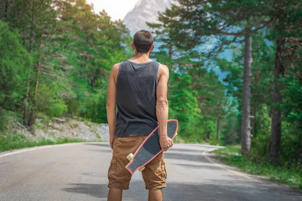 Genç hippi elinde havalı bir uzun tahta tutuyor. Güzel bir seyahat konsepti. Milenyum macera yolculuğu. Kaykay kaykay gezisi. Vahşi doğada spor.