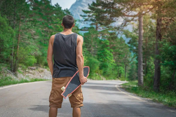 Genç hippi elinde havalı bir uzun tahta tutuyor. Güzel bir seyahat konsepti. Milenyum macera yolculuğu. Kaykay kaykay gezisi. Vahşi doğada spor.