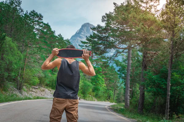 Genç hippi elinde havalı bir uzun tahta tutuyor. Güzel bir seyahat konsepti. Milenyum macera yolculuğu. Kaykay kaykay gezisi. Vahşi doğada spor.