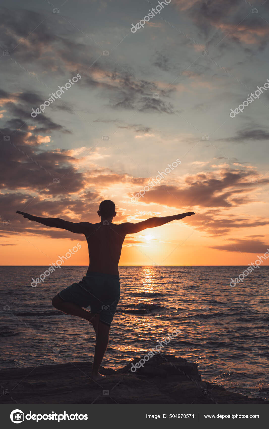 Silhouette of woman doing yoga poses outdoors on a amazing sunset while  standing on rock stock