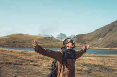Yeşil bir dağın tepesinde kolları açık genç bir adam gün batımında muhteşem göl manzarasının tadını çıkarıyor. Cennet çim dağı. Yaşam tarzı rahatlama ve özgürlük. Doğa kavramının güzelliği.