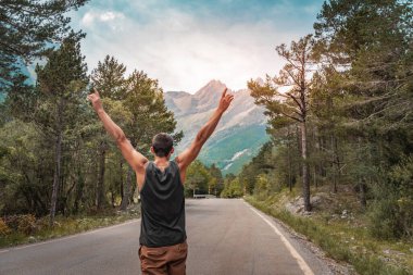 Kolları açık hippi bir adam dağ yolunda hayatın ve manzaranın tadını çıkarıyor..