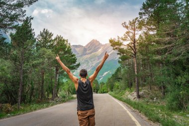 Kolları açık hippi bir adam dağ yolunda hayatın ve manzaranın tadını çıkarıyor..