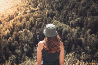 Arka planda vahşi orman dağlarıyla dışarıda tek başına duran genç bir kadın. Seyahat yaşam tarzı ve hayatta kalma konsepti. Yeşil şapkalı bir gezgin.