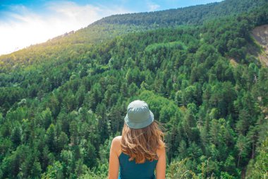 Arka planda vahşi orman dağlarıyla dışarıda tek başına duran genç bir kadın. Seyahat yaşam tarzı ve hayatta kalma konsepti. Yeşil şapkalı bir gezgin.