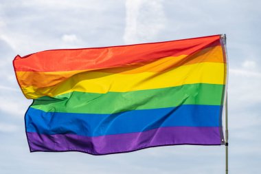 Gökkuşağı bayrağı (LGBT hareketi) güneşli mavi gökyüzü arka planında. Renkli gay bayrağı dalgalanıyor.