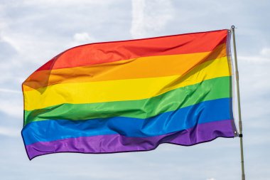 Gökkuşağı bayrağı (LGBT hareketi) güneşli mavi gökyüzü arka planında. Renkli gay bayrağı dalgalanıyor.