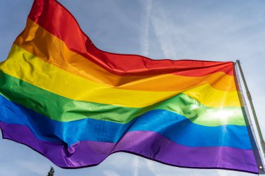 Gökkuşağı bayrağı (LGBT hareketi) güneşli mavi gökyüzü arka planında. Renkli gay bayrağı dalgalanıyor.