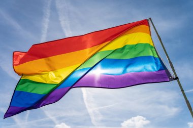 Gökkuşağı bayrağı (LGBT hareketi) güneşli mavi gökyüzü arka planında. Renkli gay bayrağı dalgalanıyor.
