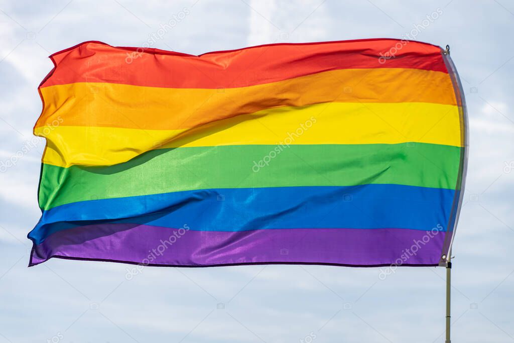 Rainbow flag (LGBT movement) on the sunny blue sky background. Colorful gay flag waving.