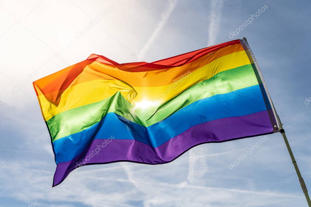 Rainbow flag (LGBT movement) on the sunny blue sky background. Colorful gay flag waving.