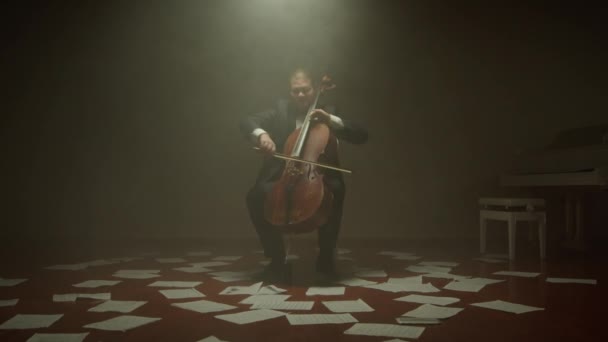 A csellista egyedül játszik a színpadon, jegyzetek a padlón. — Stock videók