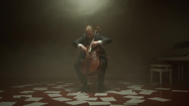 Cellisten spelar sin cello ensam på scenen, anteckningar på golvet — Stockvideo