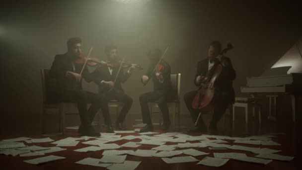 Stråkkvartetten spelar klassisk musik, Cellist spelar sin cello ensam på scen, anteckningar på golvet — Stockvideo