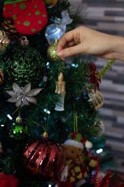 Noel mevsimi için evinin oturma odasındaki Noel ağacını süsleyen bir kadın eli.