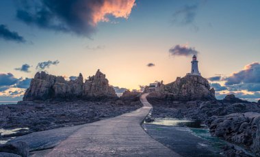 Deniz dibinde La Corbiere deniz fenerine giden yol kayalık ve günbatımında Jersey, Channel Adaları 'nın mübaşiri