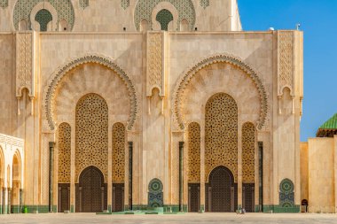 Kazablanka, Fas 'taki Hasan II Camii' nin detaylı görüntüsü geniş kemerli girişler, karmaşık geometrik fayans desenleri ve oymalı taş cepheleri gösteriyor. Mimaride geleneksel Fas mimarisi yer alıyor