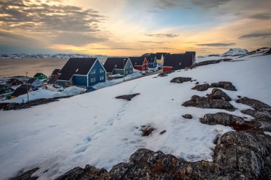 Denizin yukarısındaki karlı bir yamaçtaki renkli ahşap evler, sakin kış günbatımında geleneksel Grönland ve İnuit arktik yerleşim mimarisini gösteriyor, Nuuk, Grönland