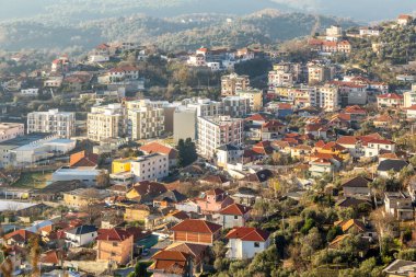 Arnavutluk 'un Kruja kenti üzerinde eğimli arazide geleneksel Arnavut evleri ve modern apartman bloklarıyla kentsel dağ manzarası düzenlendi