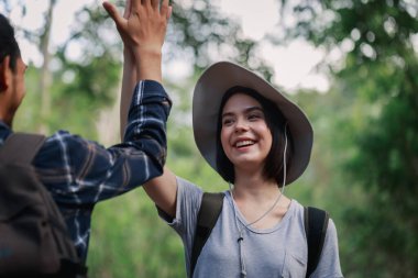Ormanda yürüyüş yapan mutlu bir çift. Aktif genç beyaz kadın yürüyüşçü Asyalı bir adamla beş el hareketi yapıyor..