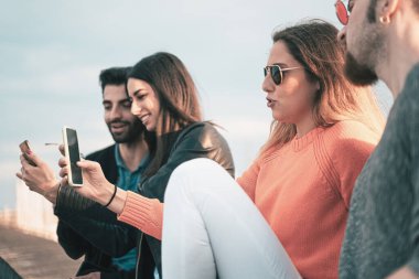 Bir grup arkadaş cep telefonlarını denize karşı kullanarak sosyal medya içeriğini izliyorlar.