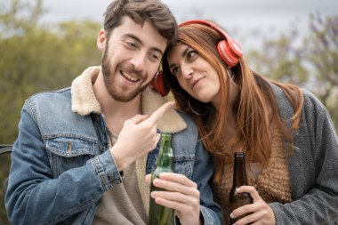 Birkaç genç, bira içiyor ve parktaki bir bankta tek başına otururken, kablosuz kulaklıklardan gelen akıllı telefon müziğini paylaşıyor..