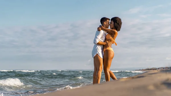 Doğada sarılıp öpüşen iki melez genç insan. Yüzler arasında güneş parlıyor. 