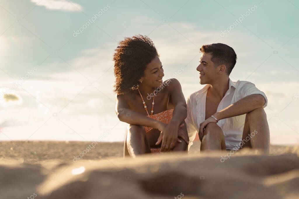 Interracial couple relaxing hugging together on a beach sitting on the sand