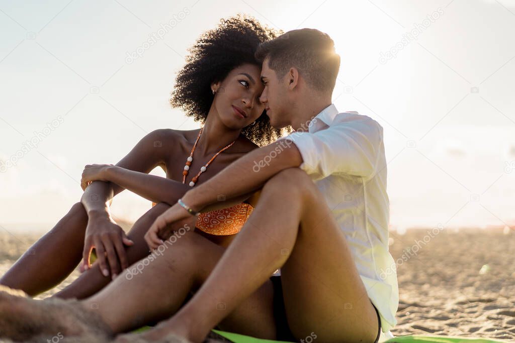 Interracial couple relaxing hugging together on a beach sitting on the sand