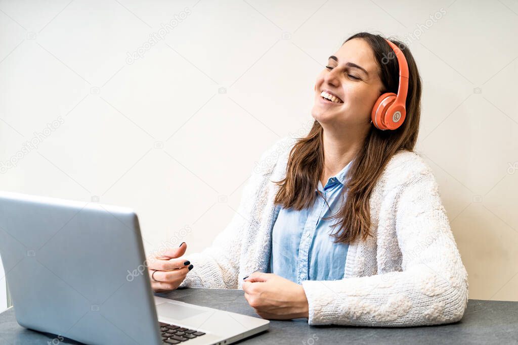 Young caucasian woman student in headphones sit on desk looking at laptop laughing on remote conference video calling