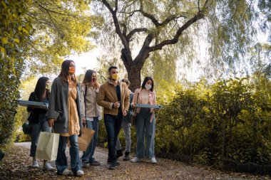 Elinde yiyecek çantaları ve pizza kutuları olan bir grup genç şehir parkında birlikte yemek yiyecekler.