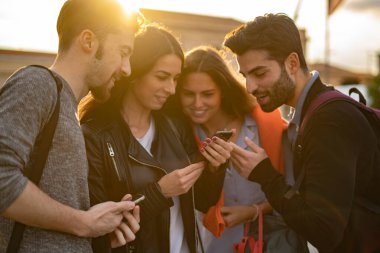 Sosyal medya uygulamasını kullanarak akıllı telefon ekranını izleyen gençler - cep telefonunu tutan ellere odaklanıyorlar