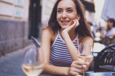 İçten gülümseyen bir kız kafede oturmuş, flört ediyor ve yazın beyaz şarap içiyor..