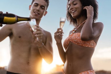 Gün batımında plajda köpüklü şarap içen genç aşıklar buluşması. Gerçek gün ışığıyla arka plan.