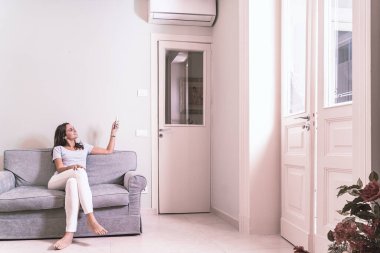 Evde klima kullanan genç bir kadın uzaktan kumandayı tutuyor.