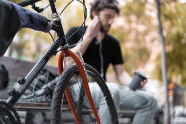 Hippi adam kenarda oturup Amerikan kahvesi içiyor ve kulaklıkla müzik dinliyor..