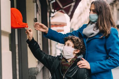 Anne ve oğlu, 2019 Coronavirus salgını yüzünden yerel bir dükkandan kuyruk bileti alıyorlar. Çocuk ve annesi yüz maskesi takıyor. COVID-19 yaşam tarzı konsepti.