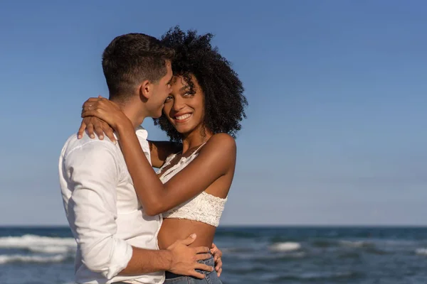 Sahilde kucaklaşan çok ırklı genç bir çift.