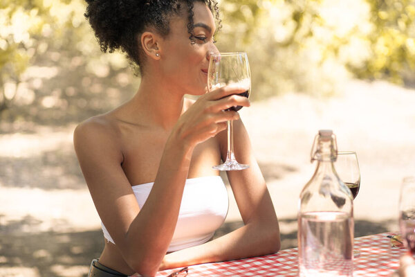 Young beautiful african descent woman drinking red wine sitting on a table in the nature