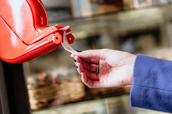 Bir kadının eli, Coronavirus salgınından dolayı sosyal mesafeyi korumak için mağazaya girmeden önce kuyruk sistemi makinesinden bilet alır.