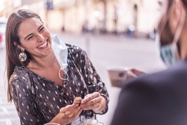 En iyi iki arkadaş açık hava kafeteryasında güvenlik maskesi açık kahve içerken eğleniyor. Coronavirus (Covid-19) Yeni normal insan yaşam tarzı kavramı.