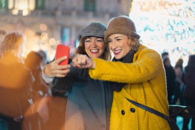 İki orta yaşlı en iyi arkadaş Noel pazarında akıllı telefon kullanarak yürüyüp eğleniyor. Yılbaşı zamanı konsepti boyunca insanlar ve arkadaşlık.