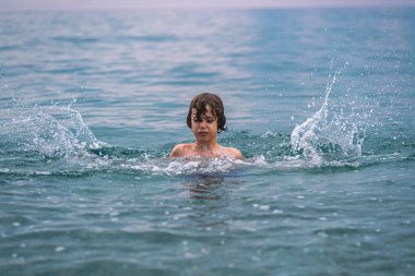 Yazın okyanusta su sıçratarak denizde oynayan bir çocuk. Suyun ortasında vuruldu.