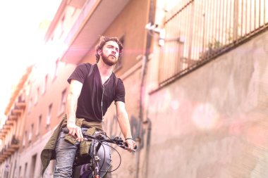 Genç sakallı adam bisikletiyle şehirde duvara çarpıyor.