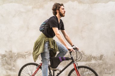 Genç sakallı adam bisikletiyle şehirde beyaz bir duvara çarpıyor.
