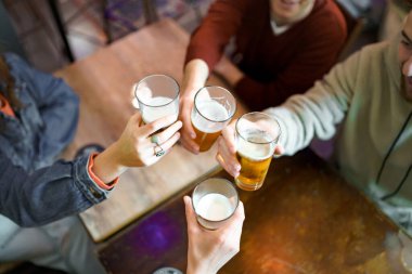 En iyi dostların barda oturup bira bardaklarını tokuşturarak kutlama kutlaması. Gençler gece konseptinde alkollü içecekler içerek eğleniyorlar.